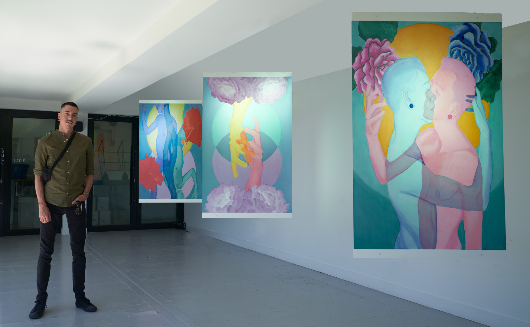 Tyler standing beside three panels of their artwork