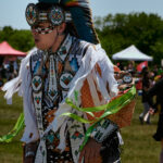 A indigenous person dancing in their ceremonial outfit outside.