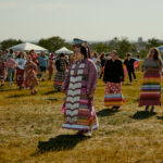 a gathering of indigenous people in their traditional garments outside on field.